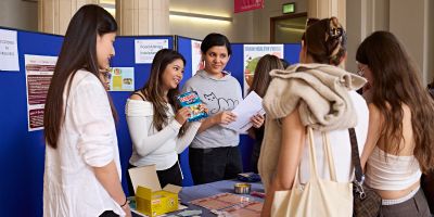 Two students showing packets of food to a crowd around a table.