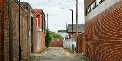 A small back alley with redbrick buildings either side and a metal fence at the back.