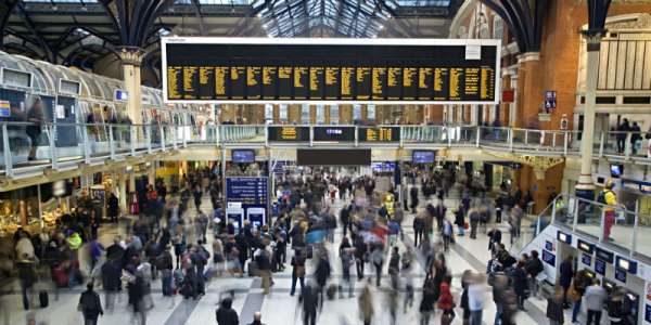 A busy and bustling train station floor featuring departure screens and lots of people moving around