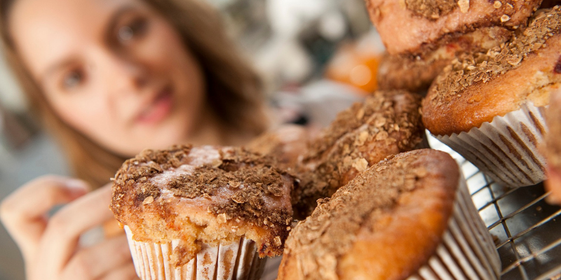 A woman looking a pile of muffins and reaching for one.