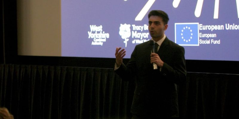 Husain Alogaily presenting, stood in front of a large screen