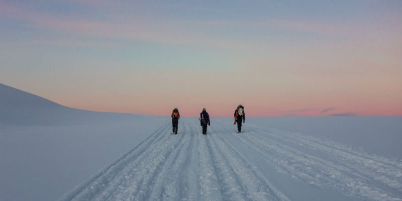 Three students walk against an icy landscape with a sunset sky