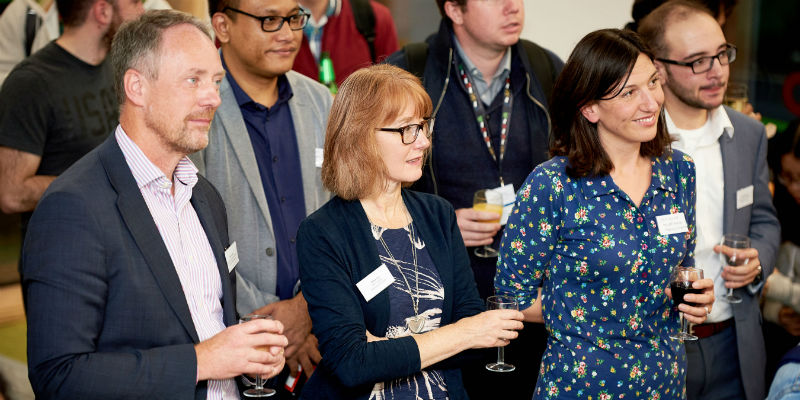 A group of adults gather at an alumni event with name badges and glasses of wine