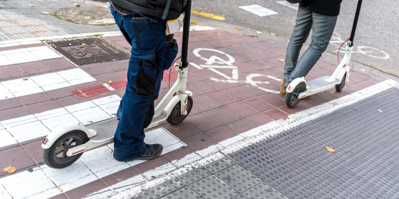 A shot from the waist down of two commuters travelling on electric scooters.