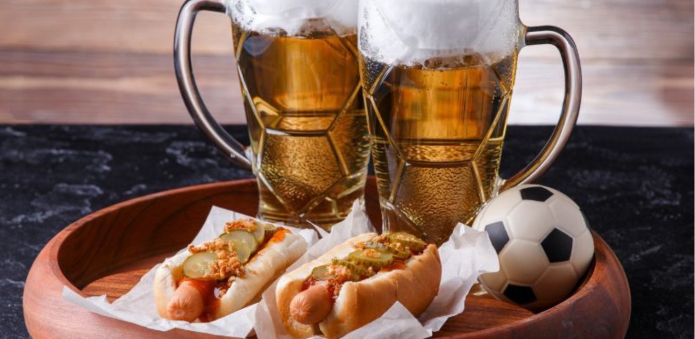 A tray with two classes of beer, two hot dogs and a mini football.