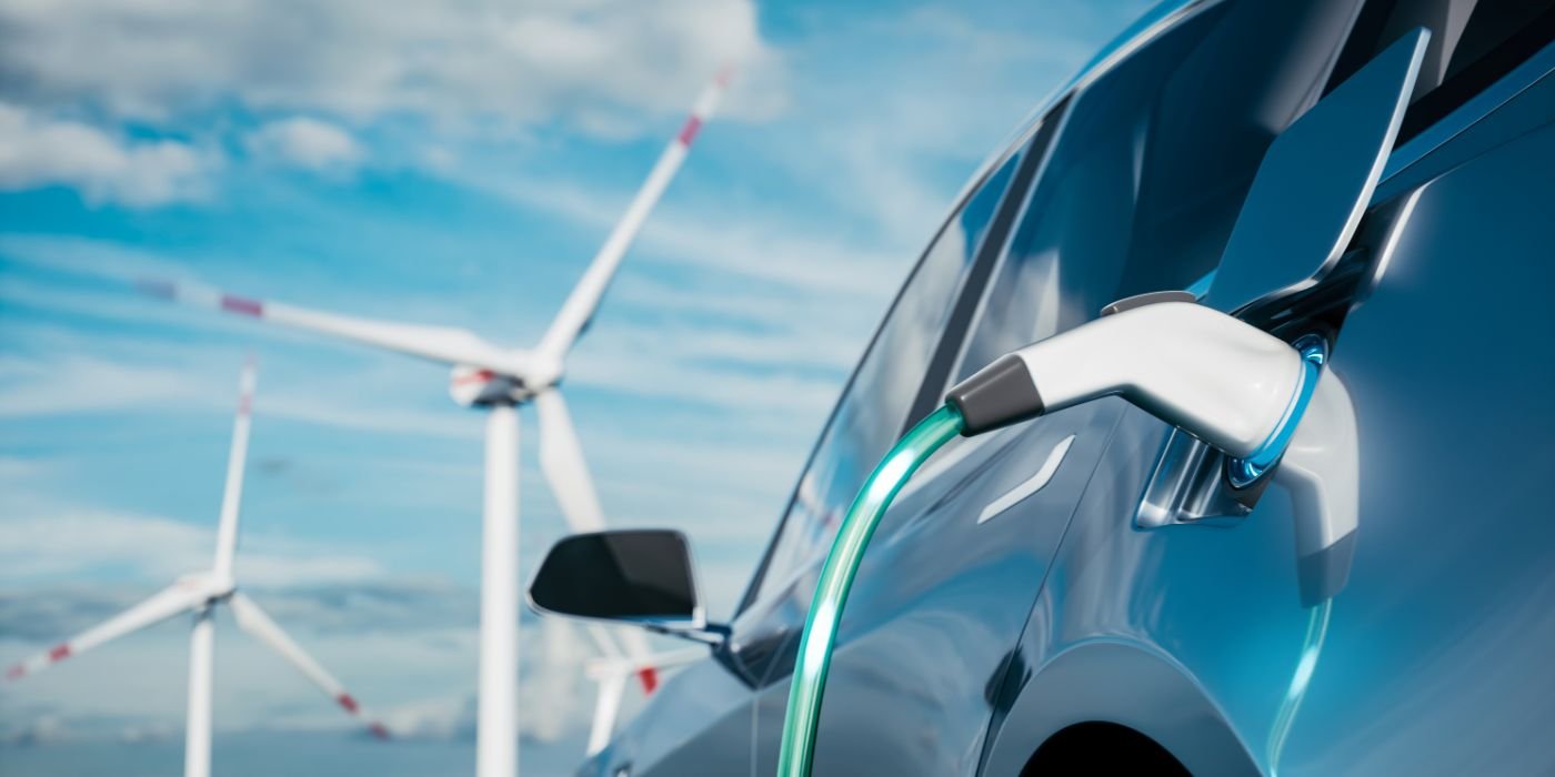 An electric car on charge, a view of wind turbines in the background.