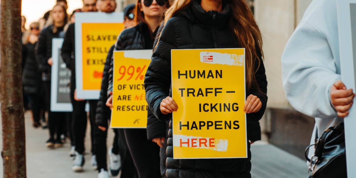 Three people holding protest signs. They read "Human trafficking happens here," "99% of victims are never rescued," and "slavery still exists."