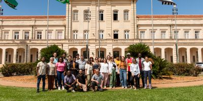 A large group of PhD students standing in front of a grand building on a sunny day