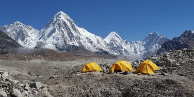 Three yellow tents at the basecamp of Mount Everest, with the snowy peaks in the background.