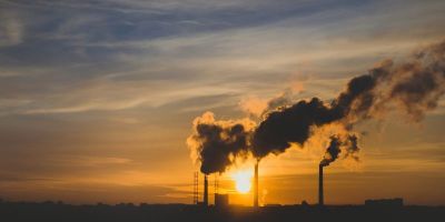 Plumes of smoke coming out of an energy plant, with the sun setting orange in the background.