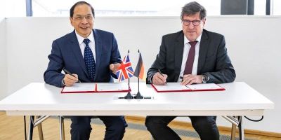 Professor Hai-Sui Yu and Professor Thomas Hirth sitting at a desk, wearing suits, each signing a contract. The Union Jack and the German Flag are in small flag holders on the table.