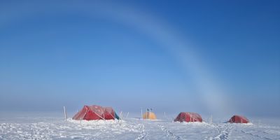 Four red tents on the ice field, with a wide blue sky above.