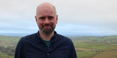 Professor Chris Davies, smiling, in front of a landscape of fields and hills.