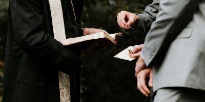 A cropped photo of two men getting married in a church, as they exchange rings.