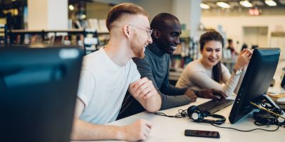 Three people sitting at a desktop computer, smiling