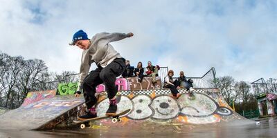 Skateboarder performing tricks in a skatepark with other skateboarders watching in the background.