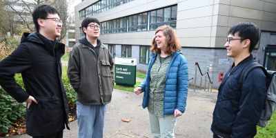 Three postgraduate researchers and their supervisor stood outside the School of Earth and Environment building, laughing together