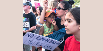 Some people at a protest in the USA. Sign reads: No human being is illegal.