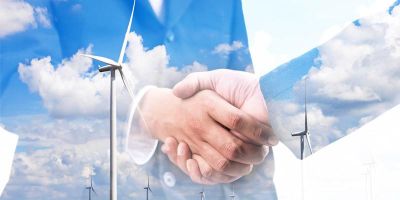 Stock image of two business men shaking hands with low transparency, over the image is a wind farm.