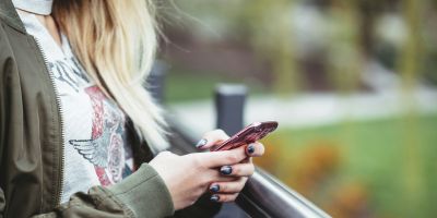 A close up of someone's hands holding their phone. Greenery can be seen in the background.