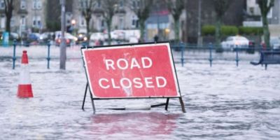 A "Road Closed" sign on a street that's covered in floodwater.