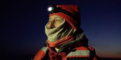 a photo of Professor Ian Brooks wrapped up in a wool hat with a head torch, scarf and warm jacket, against a dark sky.