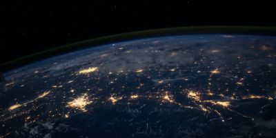 A picture of the Earth at night from space. Some areas of land are lit up with lights.
