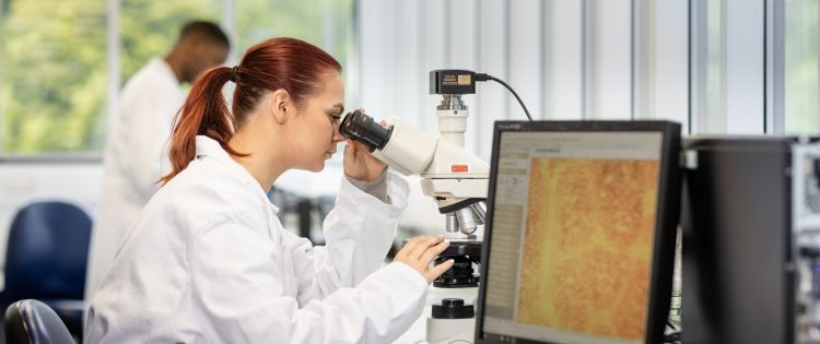Image of a female geography student in the lab using a microscope.