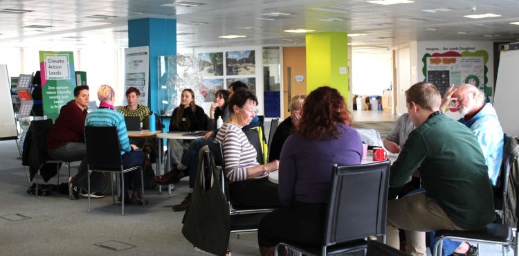 Two tables of people talking, with a Climate Action Leeds banner in the background