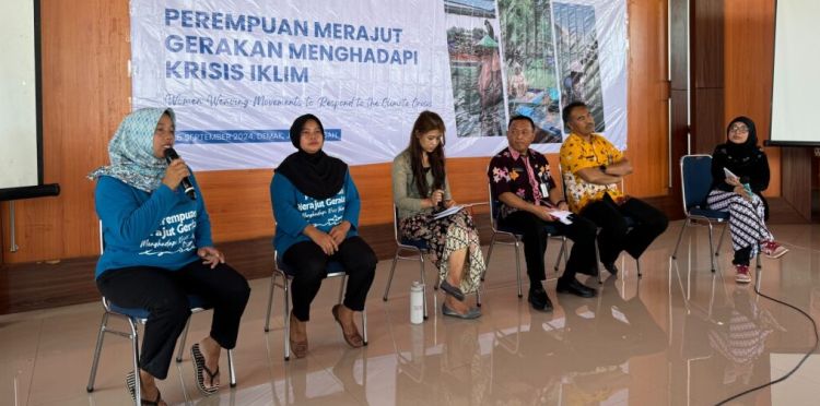 Six people sitting on a stage, one speaking into a microphone.