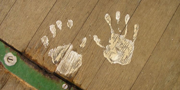 Two muddy handprint on a wooden floor.