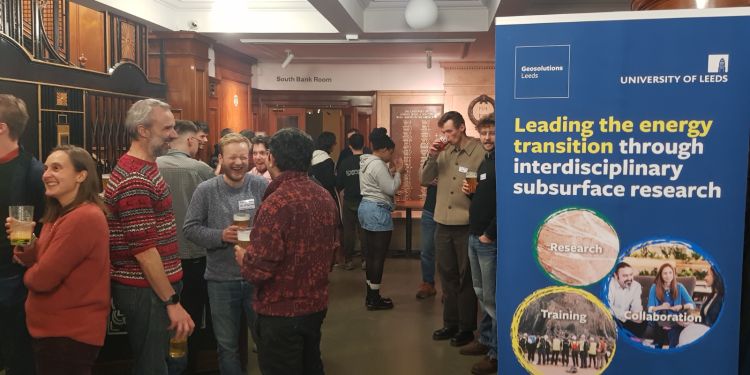 People chatting with drinks in their hands. A poster on the right reads "leading the energy transition through interdisciplinary subsurface research"