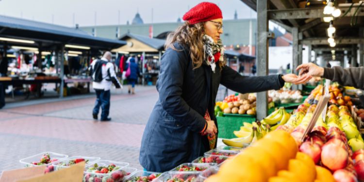 Someone in a red hat at a fruit and vegetable stall in an outdoor market.