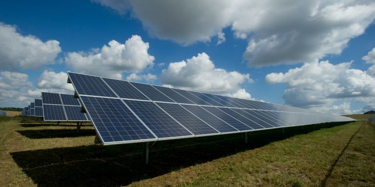 A field of solar panels under a blue, cloudy sky