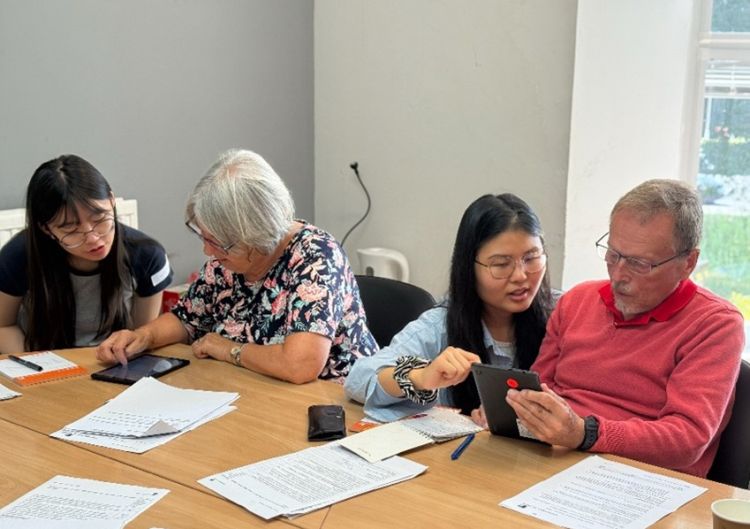 four people sit at a table using technology to record data