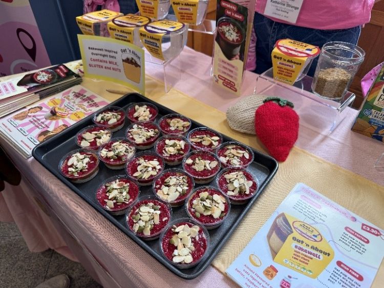 Team Oat 'N About's products on display. The product, overnight oats, is pink with an almond topping and is in small cups. 