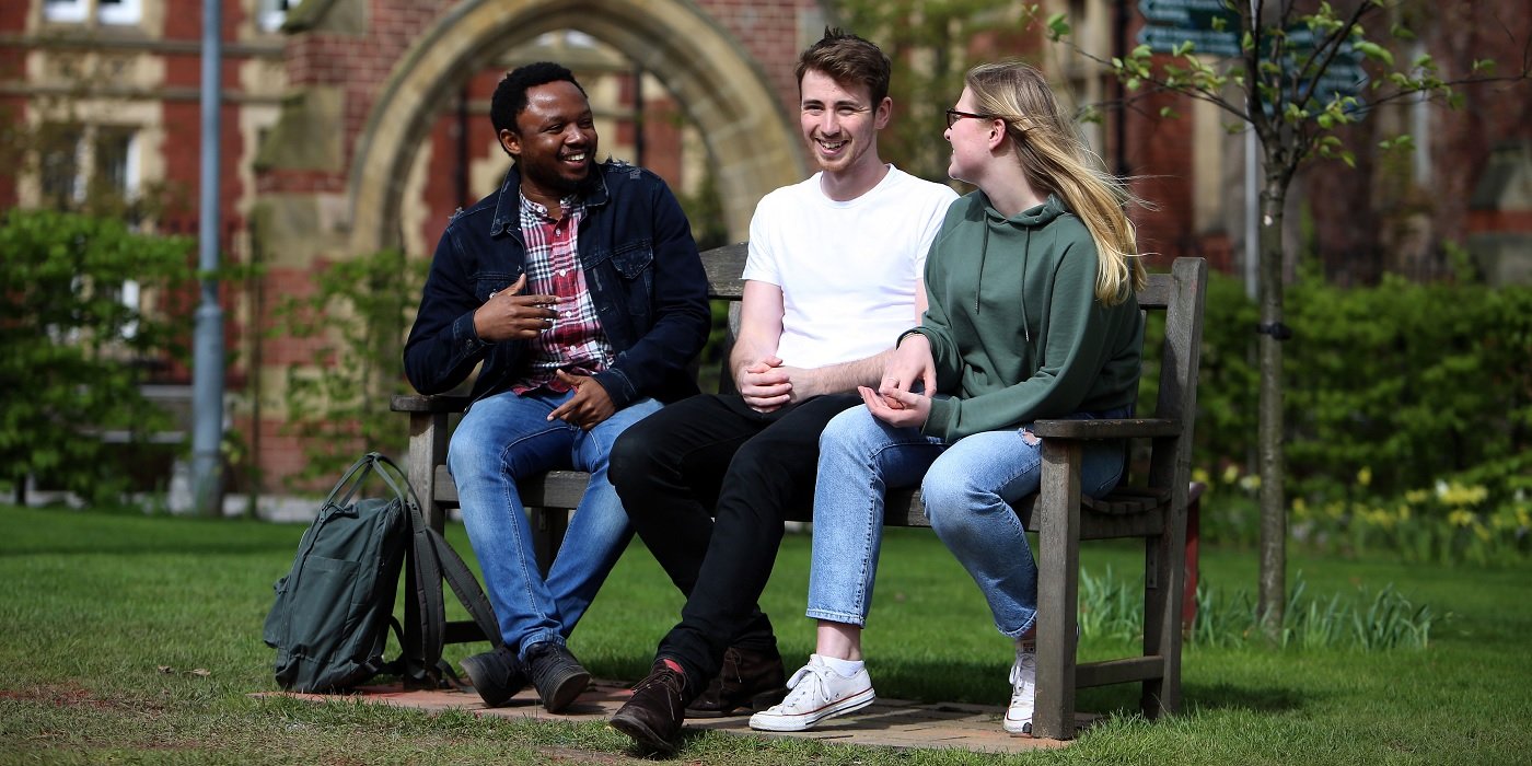 Three students sat on a bench, in the background is the University of Leeds' Great Hall.