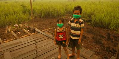 Two children stood in a field wearing green masks across their faces.