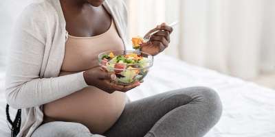 Pregnant woman sitting cross-legged eating salad