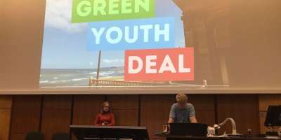 Two student speakers at the podium in front of a screen promoting the Green Youth Deal