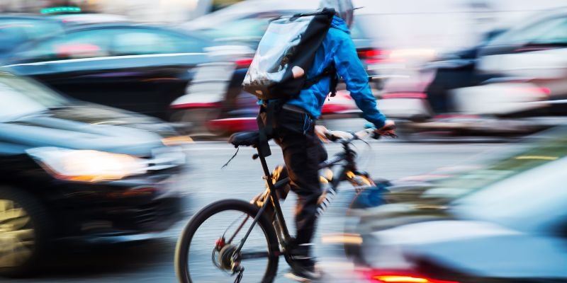 Cyclist riding along a busy street with blurred cars in the background